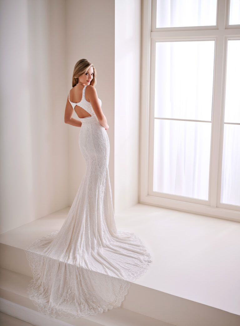 Back view of the E403 ivory mermaid bridal gown showing the open back and long lace train beside a window
