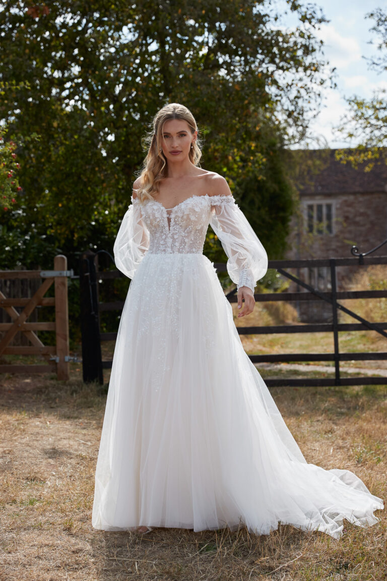 Full-length front view of the Easton ivory A-line bridal gown with lace bodice and long sheer sleeves outdoors