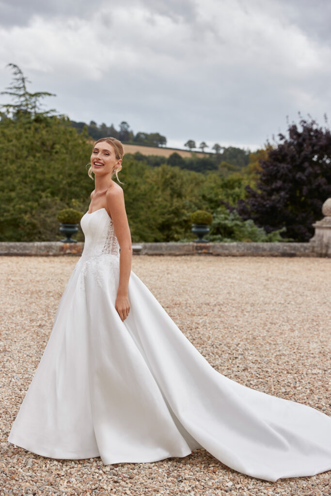 Bride wearing the Lake ivory ball gown, holding its full satin skirt outdoors