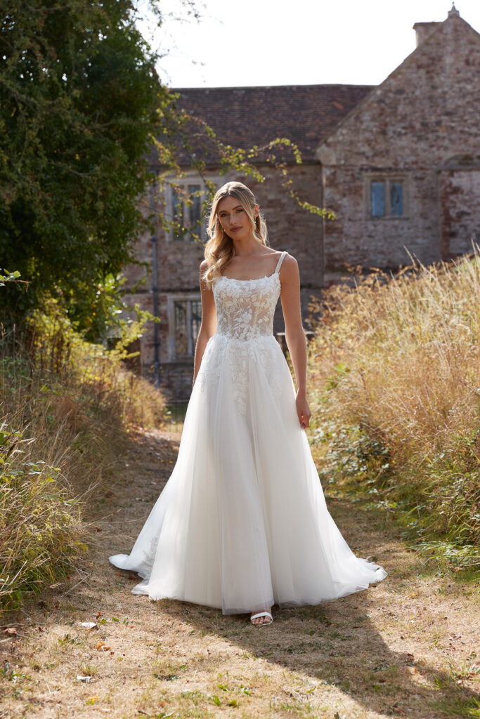 Full-length front view of the Marlie ivory A-line bridal gown with lace bodice outdoors by a stone building