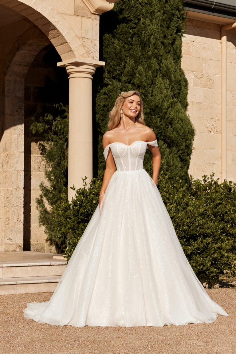 Full-length front view of the Lazaris Y3103 ivory ball gown with off-the-shoulder corset bodice outdoors